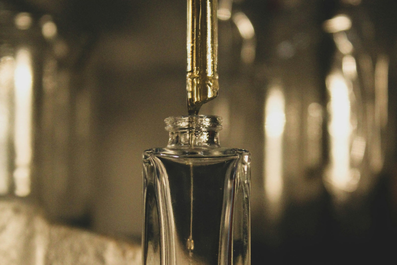 A glass perfume bottle being filled with warm honey-toned fragrance in soft golden light