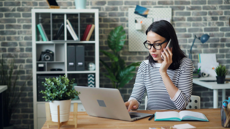 Woman at her desk on a call, working on a laptop and taking notes during a strategy session