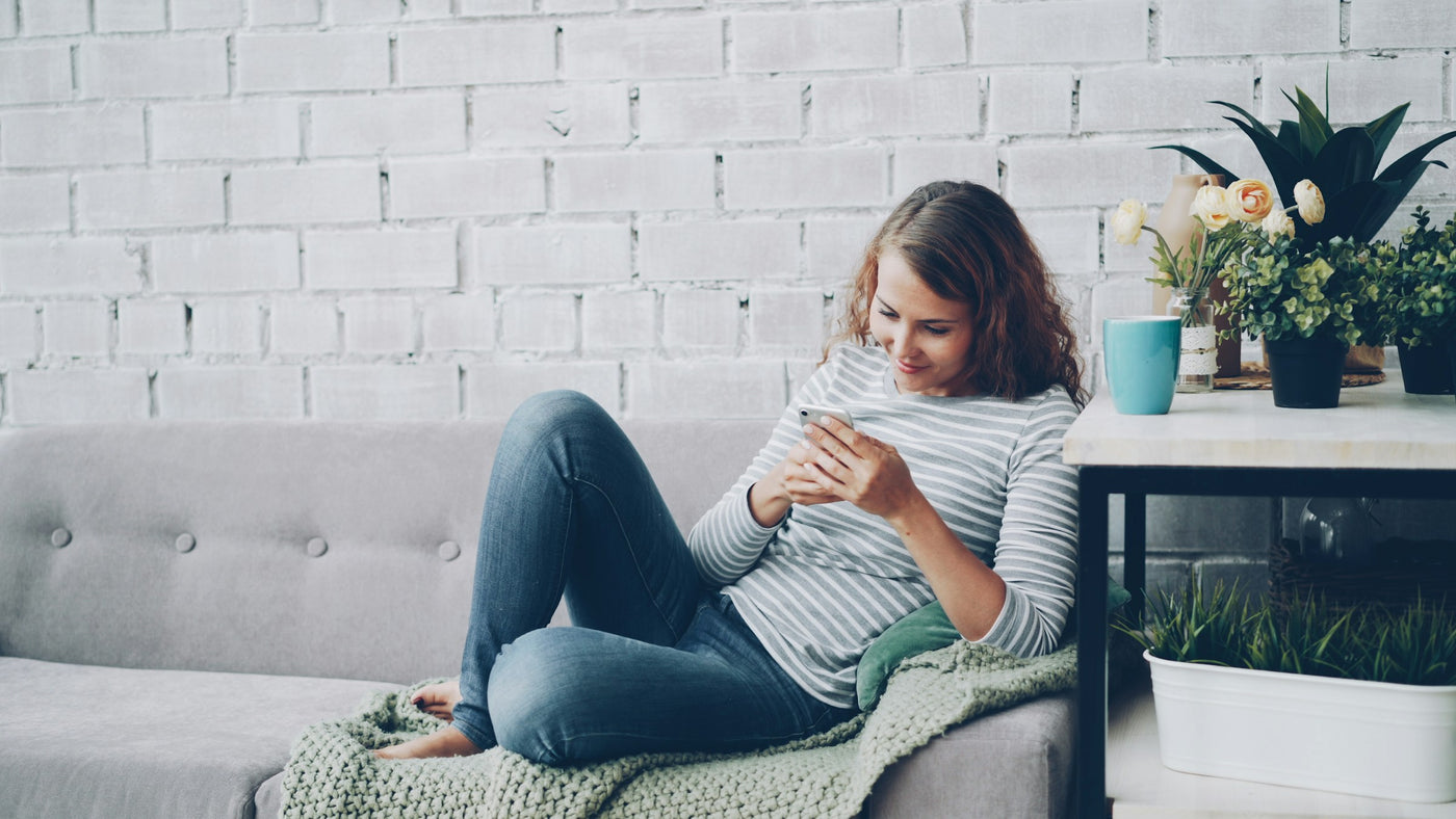 Woman on a comfortable sofa smiling at her smartphone in a warm cozy home