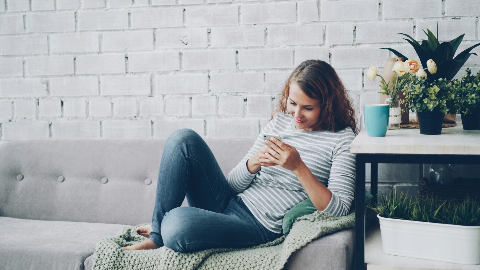 Woman on a comfortable sofa smiling at her smartphone in a warm cozy home