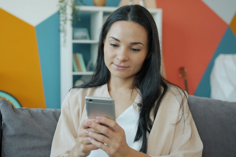 A woman relaxing on a couch in a warm, softly lit room, looking at her phone