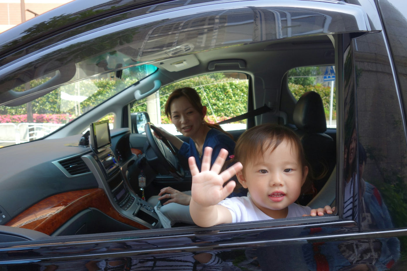 Child waving from the car window while mom drives on a summer road trip