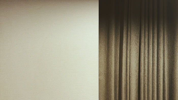 Warm shadow and light falling across a cream wall beside a brown curtain